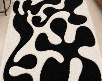 May include: A rectangular area rug featuring a high-pile texture with a bold, abstract pattern of interconnected black organic shapes set against a solid white background. The design consists of fluid, blob-like forms that span the entire surface.