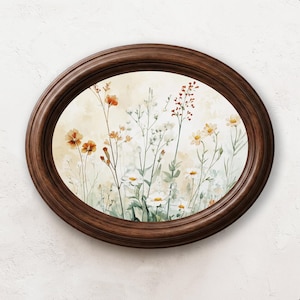 Könnte beinhalten: Ein ovales Wandbild mit einer Aquarellillustration von Wildblumen in Orange-, Weiß- und Grüntönen. Das Kunstwerk ist in einem dunkelbraunen Holzrahmen mit glattem, abgerundetem Profil gefasst und befindet sich an einer strukturierten weißen Wand.