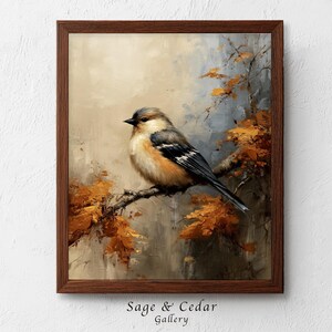 Könnte beinhalten: Ein gerahmtes Ölgemälde eines kleinen Vogels mit braunen, weißen und schwarzen Federn, der auf einem Ast sitzt. Der Vogel ist von herbstlich orangefarbenen und goldenen Blättern vor einem weichen, neutralen Hintergrund umgeben. Der Text Sage & Cedar Gallery ist sichtbar.