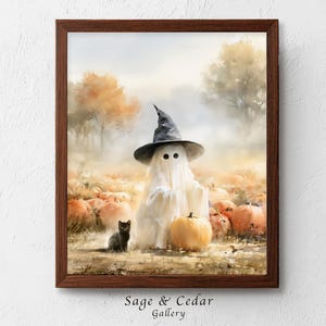 Könnte beinhalten: Ein gerahmter Kunstdruck, der einen Geist mit einem schwarzen Hexenhut in einem Kürbisfeld mit einer kleinen schwarzen Katze zeigt. Die Szene spielt in einer herbstlichen Landschaft mit orangefarbenen Bäumen und Nebel. Text Sage & Cedar Gallery unten.