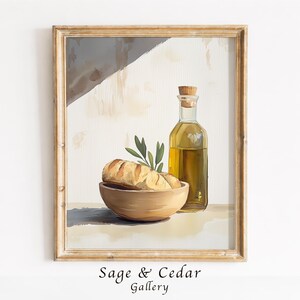Könnte beinhalten: Ein gerahmter Druck im Aquarellstil zeigt eine Holzschale mit einem Laib knusprigem Brot und einem Zweig mit grünen Blättern, neben einer klaren Glasflasche mit goldenem Olivenöl, alles vor einem neutralen Hintergrund dargestellt.