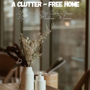Puede incluir: Naturaleza muerta con un jarrón blanco con flores secas, un dispensador de jabón blanco y el texto "A CLUTTER - FREE HOME". La imagen está sobre una mesa de madera.