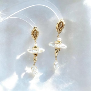 May include: A pair of gold-toned drop earrings featuring an ornate, textured oval top piece, a central horizontal white baroque pearl, and a small dangling white pearl at the bottom, all connected by polished gold metal links and components.