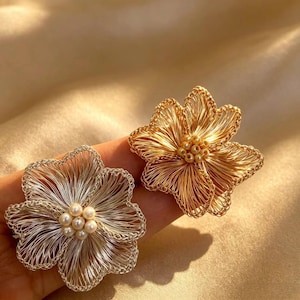 May include: Two flower-shaped brooches, one in silver-tone wire and one in gold-tone wire. Each brooch features a cluster of small, round, cream-colored faux pearls at the center, surrounded by delicate, multi-layered wire petals in a floral design.