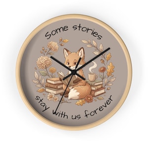 Könnte beinhalten: Runde Wanduhr mit hellem Holzrahmen. Das Zifferblatt zeigt einen Cartoon-Fuchs, der ein Buch liest, umgeben von Büchern, Blumen und dem Text "Some stories stay with us forever."
