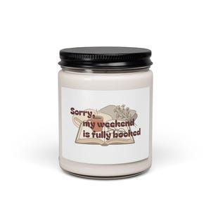 Könnte beinhalten: Ein weißes Kerzenglas mit schwarzem Deckel. Das Etikett zeigt eine Illustration eines Buches, einer Kaffeetasse und Blumen mit dem Text "Sorry, my weekend is fully booked" in braunen Buchstaben. Die Kerze ist ein Einrichtungsgegenstand.