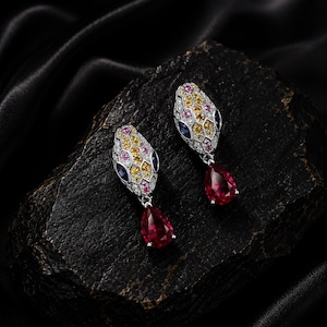 Peut inclure: Une paire de boucles d'oreilles pendantes en forme de serpent avec un motif en nid d'abeille serti de pierres jaunes, roses et blanches. Chaque boucle possède une pierre bleu foncé pour l'œil et une grosse gemme rouge en forme de poire.