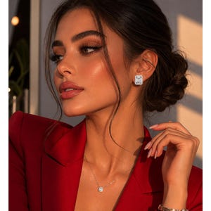 May include: A woman in a red blazer, wearing diamond stud earrings and a diamond pendant necklace. The earrings and necklace feature square-cut diamonds. The woman has dark hair and is wearing makeup.