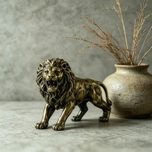 May include: A bronze-colored lion statue in a roaring pose. The sculpture has detailed features, including a textured mane and open mouth. A beige vase with dried grass is in the background, adding a decorative element to the scene.