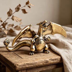 May include: A brass dragon figurine with outstretched wings and an open mouth, posed on a wooden surface. The dragon has detailed scales and a curved tail. The figurine is a decorative item.