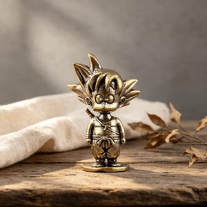 May include: A small, metallic bronze-coloured figurine of a cartoon character with spiky hair, large round eyes, and a small nose. The character wears a martial arts-style outfit with a sash at the waist and a thin strap across the chest, standing on a base.