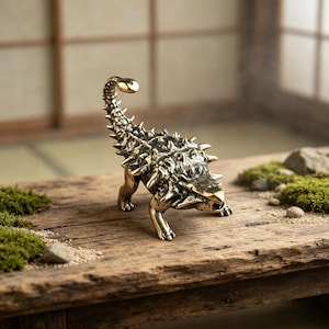 May include: A detailed brass Ankylosaurus dinosaur figurine. The sculpture features a textured surface with spikes and a curved tail. The dinosaur is posed on a wooden surface, showcasing its intricate design and metallic finish.