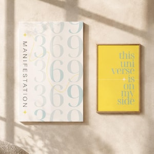 May include: Two rectangular wall art prints. The left print is off-white with the vertical text MANIFESTATION, a thin yellow line, and the repeating light blue number sequence 369. The right print is yellow with the blue text this universe is on my side.