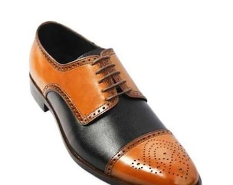 Puede incluir: Un zapato oxford bicolor con empeine y paneles laterales de cuero negro contrastados con cuero color canela en la puntera y la cordonera. El zapato incluye perforaciones decorativas tipo brogue a lo largo de la puntera y las costuras, con cordones marrones.