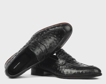 Puede incluir: Un par de mocasines negros con un acabado de cuero texturizado estilo avestruz. Los zapatos tienen un diseño clásico sin cordones con punta redondeada y tacón bajo. La plantilla interior muestra claramente el nombre de marca Valerio Veneto en blanco.