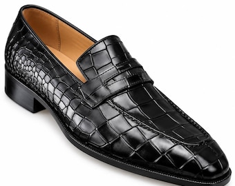 Puede incluir: Un zapato tipo mocasín negro sin cordones con una textura brillante en relieve de piel de cocodrilo en la parte superior. El zapato presenta una tira clásica de mocasín sobre el empeine, punta redondeada, tacón bajo y forro interior color canela.