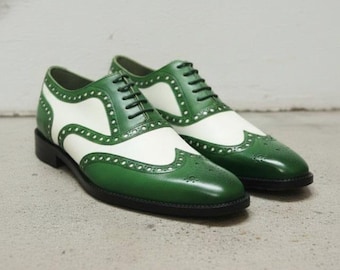 Puede incluir: Un par de zapatos oxford de estilo wingtip en dos tonos, con una parte superior de cuero en color verde vibrante y blanco hueso. Los zapatos incluyen perforaciones decorativas tipo brogue a lo largo de las costuras, cordones negros y suela.