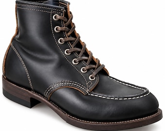 Puede incluir: Un botín de cuero negro con puntera estilo mocasín y costuras blancas en contraste, ojales metálicos plateados, cordones de color marrón oscuro y un tacón y suela de color marrón oscuro con construcción de vira visible.