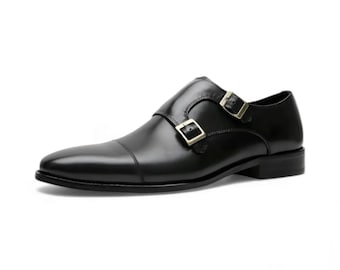 Puede incluir: Un zapato de doble hebilla en cuero negro con puntera, acabado pulido liso y dos hebillas metálicas en el lateral. El zapato tiene un tacón bajo y una silueta estructurada, mostrando una apariencia limpia y formal.