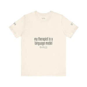 Op de afbeelding: Crèmekleurig T-shirt met de zwarte tekst "my therapist is a language model". Het ontwerp bevat een bank en een laptop-icoon. De merknaam "ILAYA" staat op de mouwen.