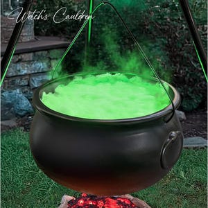 May include: A black cauldron hanging from a tripod stand, filled with glowing green light and textured material. The text "Halloween Decorations Witch's Cauldron" is visible at the top. Below the cauldron, a pile of glowing red faux embers sits.