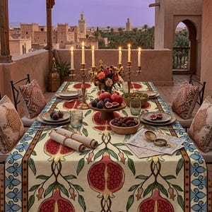 Peut inclure: Une nappe rectangulaire ornée d'un motif répétitif de grenades rouges et de feuilles vertes sur fond crème, bordée d'un design géométrique bleu et marron. La table est dressée avec des assiettes, des bols de fruits, des bougies et des parchemins.
