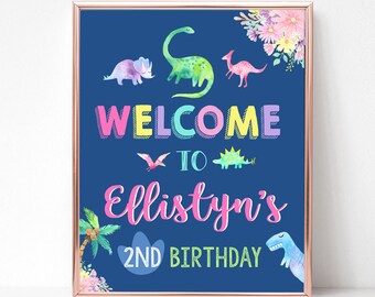 May include: A blue welcome sign with a pink dinosaur and the text "WELCOME TO Ellistyn's 2ND BIRTHDAY". The sign is decorated with colorful flowers and a palm tree.