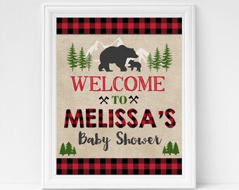 Puede incluir: Un letrero enmarcado para baby shower con un tema rústico. El letrero presenta una silueta de oso negro y osezno, pinos y las palabras "WELCOME TO MELISSA'S Baby Shower" en letras a cuadros rojas y negras. El letrero está enmarcado en blanco.