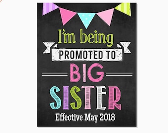 May include: A chalkboard sign with colorful bunting at the top. The sign says "I'm being promoted to BIG SISTER Effective May 2018".