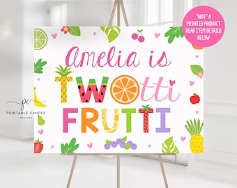 May include: A white printable sign with the text "Amelia is Twotti Frutti" in colorful letters with fruit illustrations. The sign is decorated with hearts, fruit, and leaves.