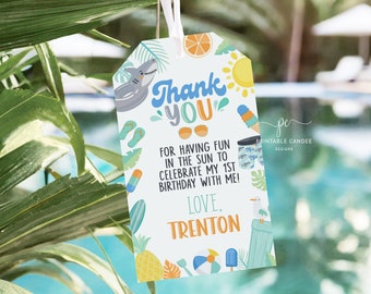 May include: A white thank you tag with a blue and green tropical theme. The tag features a shark, sunglasses, a pineapple, a beach ball, and an ice cream cone. The text on the tag reads "Thank You" and "For having fun in the sun to celebrate my 1st birthday with me! Love, Trenton".