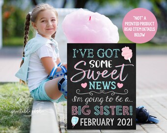 May include: A chalkboard sign with the text "I've got some sweet news I'm going to be a... Big Sister! February 2021". The sign is decorated with pink and blue hearts and a pink cotton candy graphic.