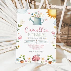 Könnte beinhalten: Eine farbenfrohe Einladung zu einer ersten Geburtstagsfeier mit Garten-Thema. Die Einladung zeigt eine Gießkanne mit Blumen, einen Pilz und eine Schnecke. Der Text auf der Einladung lautet "Camellia wird eins, bitte feiern Sie mit uns, 13. August, von 14:00 bis 16:00 Uhr, Camellia's Garden Center, 3464 Sunflower Street, Ferndale, WA, RSVP an 134-467-2465."