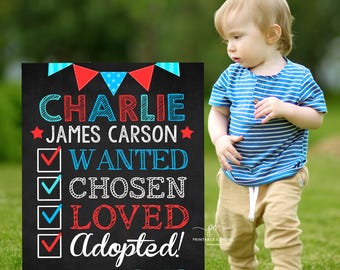 May include: A black chalkboard sign with red and blue bunting at the top. The sign says "CHARLIE JAMES CARSON" and has a checklist with the words "WANTED", "CHOSEN", "LOVED", and "Adopted!" checked off. The date "NOVEMBER 15, 2025" is at the bottom of the sign.