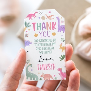 Puede incluir: Una etiqueta de agradecimiento de tem&aacute;tica de dinosaurios rosa y verde con el texto "THANK YOU" y "FOR STOMPING BY TO CELEBRATE MY 2ND BIRTHDAY WITH ME! Love, EMERSYN".