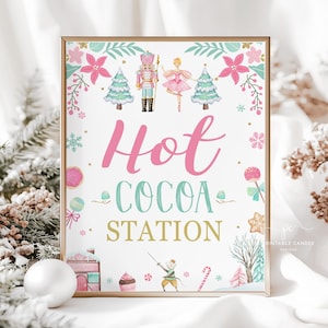 May include: A framed sign with a gold border, featuring the words "Hot Cocoa Station" in pink, teal, and gold. The sign is decorated with illustrations of a nutcracker, ballerina, Christmas trees, and other festive elements. The background is white.