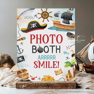 May include: A printable photo booth sign with a pirate theme. The sign features a pirate hat, a treasure chest, a ship, and a cannon. The text on the sign reads "Photo Booth Arrrr Smile!"