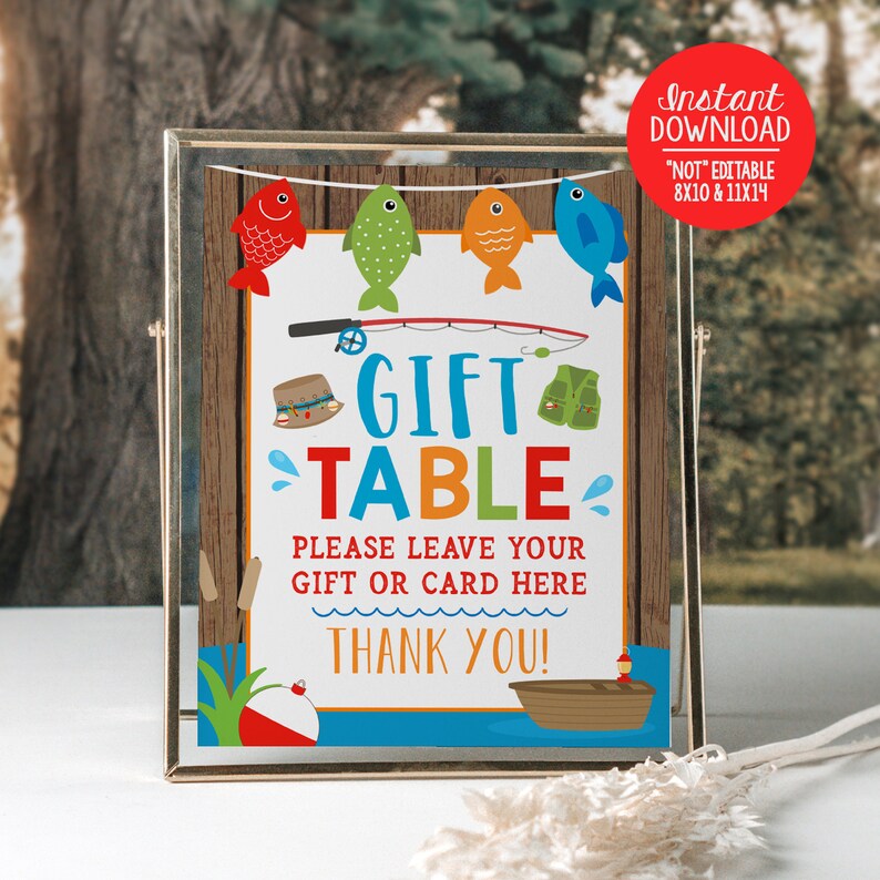 K&ouml;nnte beinhalten: Ein druckbares Schild f&uuml;r einen Geschenketisch mit einem Angelthema. Das Schild hat einen blauen, gr&uuml;nen und orangen Hintergrund mit einem Holzrahmen. Es steht "Gift Table" in gro&szlig;en Buchstaben und "Please leave your gift or card here" in kleineren Buchstaben. Das Schild hat auch eine Angelrute, Fische und einen K&ouml;der.