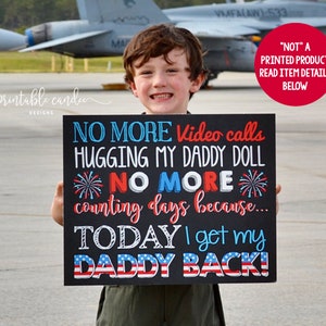 Puede incluir: Un niño sostiene un letrero negro de pizarra con el texto "NO MORE Video calls HUGGING MY DADDY DOLL *NO MORE* counting days because... TODAY I get my DADDY BACK!" El letrero tiene estrellas y fuegos artificiales rojos, blancos y azules.