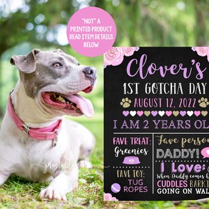May include: A black chalkboard sign with pink and gold floral accents. The sign says "Clover's 1st Gotcha Day August 12, 2022 I am 2 years old" and includes details about the dog's favourite treats, person, and activities.
