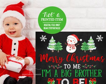May include: A black chalkboard sign with a snowman and Christmas trees. The sign says "Merry Christmas to me I'm a big brother to be!"  The sign is decorated with red and green Christmas decorations.