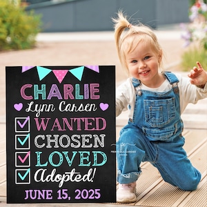 Op de afbeelding: Een zwart schoolbordteken met de tekst "CHARLIE Lynn Carsen" in roze en blauwe letters. Het bord bevat ook een checklist met de woorden "WANTED", "CHOSEN", "LOVED" en "Adopted!" in roze en blauw. De datum "JUNE 15, 2025" staat in paars onderaan het bord.