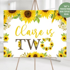 Könnte beinhalten: Ein weißes bedruckbares Schild mit einem Sonnenblumenrand. Der Text "Claire is Two" ist in Braun und Gelb geschrieben. Das Schild steht auf einem Staffelei.