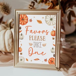May include: A gold-framed sign with a white background and fall-themed decorations. The sign says "Favors Please Take One" in brown text. There are pumpkins, leaves, and flowers on the sign.