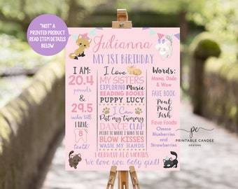 May include: Pink and purple first birthday sign with a cat theme. The sign says "Julianna My 1st Birthday" and includes details about the child's age, weight, height, and favorite things. The sign also includes a cute illustration of a cat.