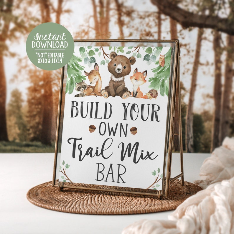 May include: A printable sign with a woodland theme featuring a bear, fox, raccoon, and deer. The sign says "Build Your Own Trail Mix Bar".