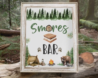 Op de afbeelding: Een printbaar bord voor een s'mores bar met een aquarel achtergrond van een bos. Het bord zegt "S'mores Bar" met een afbeelding van een s'more, een tent, een lantaarn, een kampvuur en een beer.