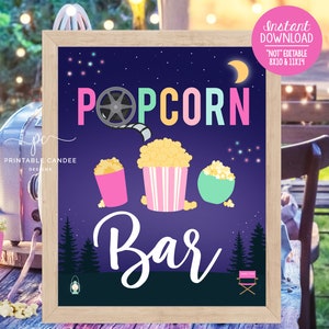May include: A framed sign with a dark blue background features the words "Popcorn Bar" in colorful letters. Illustrations of popcorn in pink, striped, and green containers are below the text. The sign includes a film reel graphic and a crescent moon.