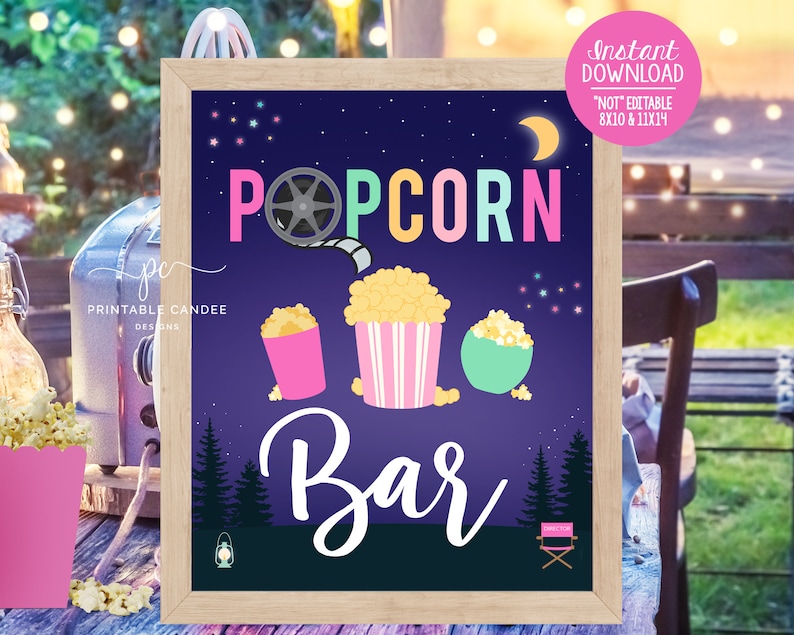 May include: A framed sign with a dark blue background features the words "Popcorn Bar" in colorful letters. Illustrations of popcorn in pink, striped, and green containers are below the text. The sign includes a film reel graphic and a crescent moon.