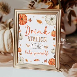 May include: A printable sign with a gold frame and a white background. The sign features a fall theme with pumpkins, leaves, and flowers. The text on the sign reads "Drink Station Please help yourself".